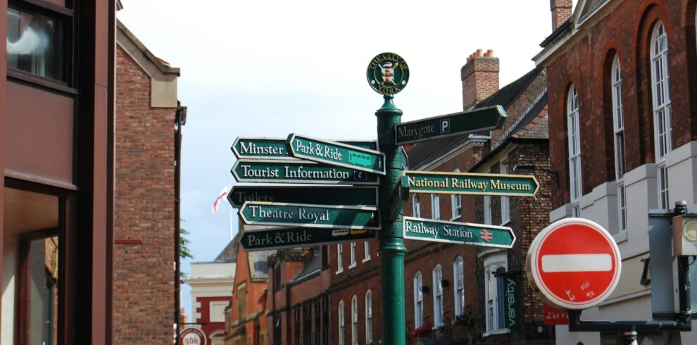 Viva newyork Street signs in historic York city center, England, with brick buildings and blue sky.